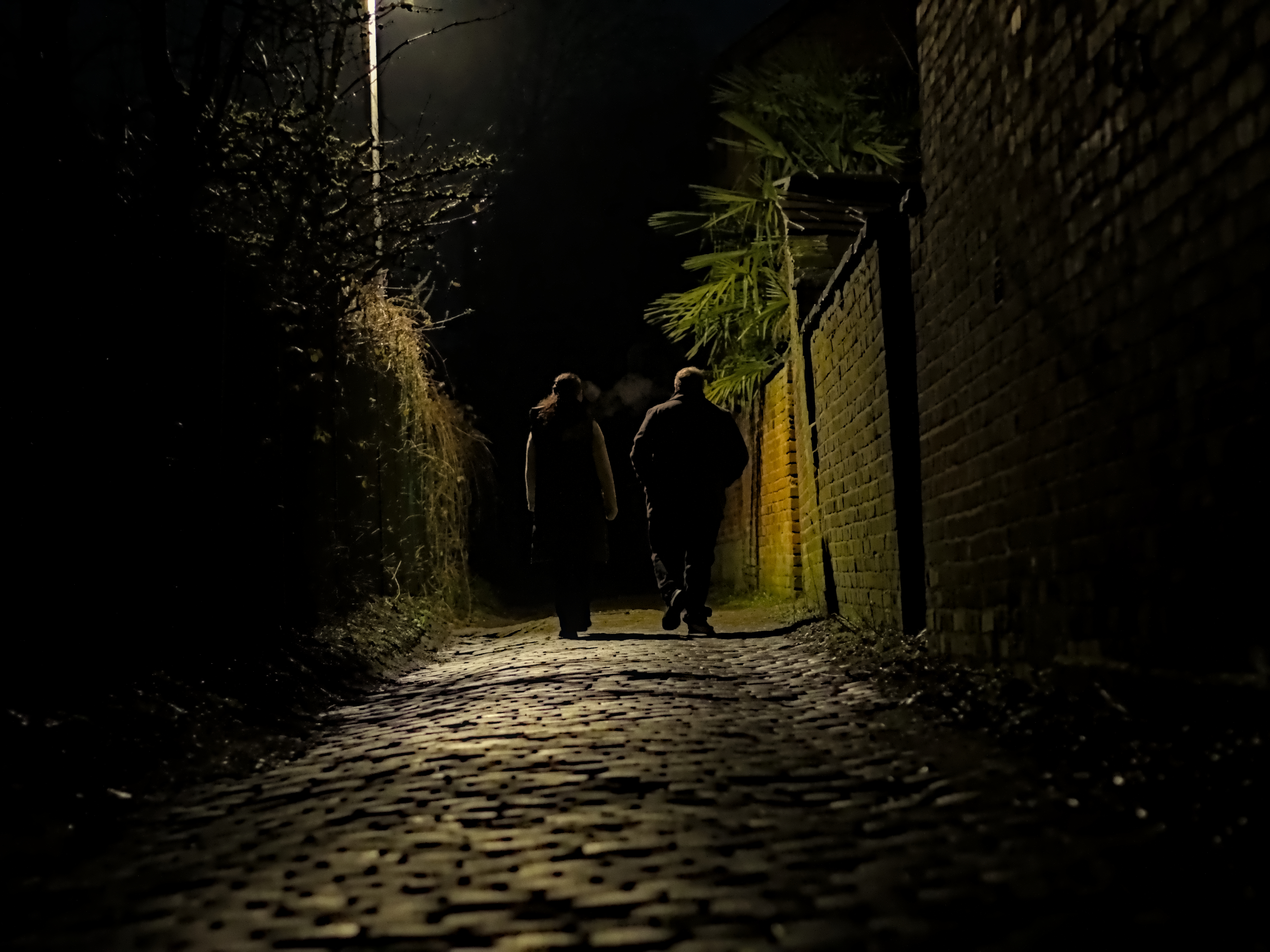 A moody image of 2 people walking in a dimly lit alley way